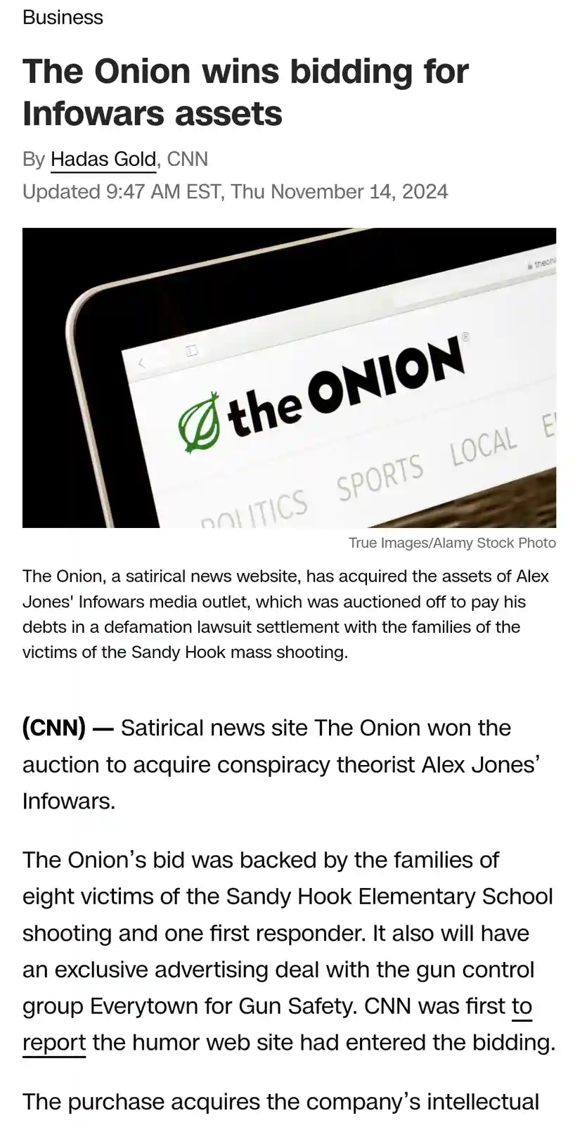 A screenshot of a CNN news article titled 'The Onion wins bidding for Infowars assets' shows a tablet displaying The Onion's…
