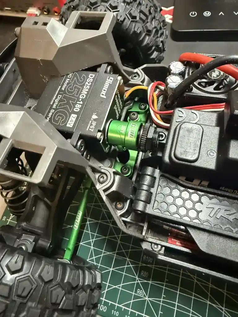 A close-up photo of the internals of a remote-controlled car, showing a black motor labeled 'DS25MG-180 25KG' mounted on a…