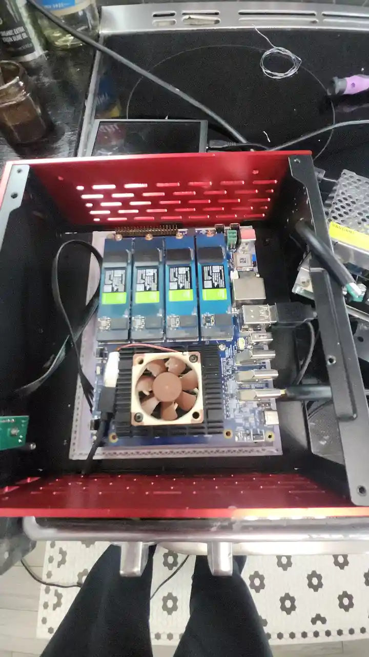 An overhead view of a custom-built computer case with a red perforated top panel, revealing a motherboard with four blue M.2…