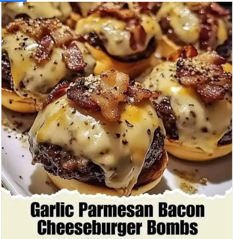 A close-up photo of several small, round cheeseburger bombs on buns, each topped with melted cheese, crispy bacon bits, and…