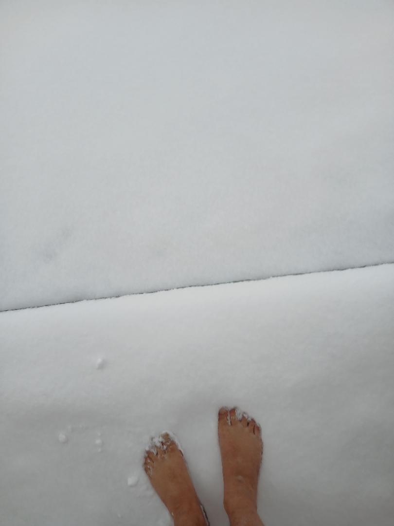 A top-down view shows a person's bare feet standing in snow, with snowflakes clinging to their toes. The image is split…