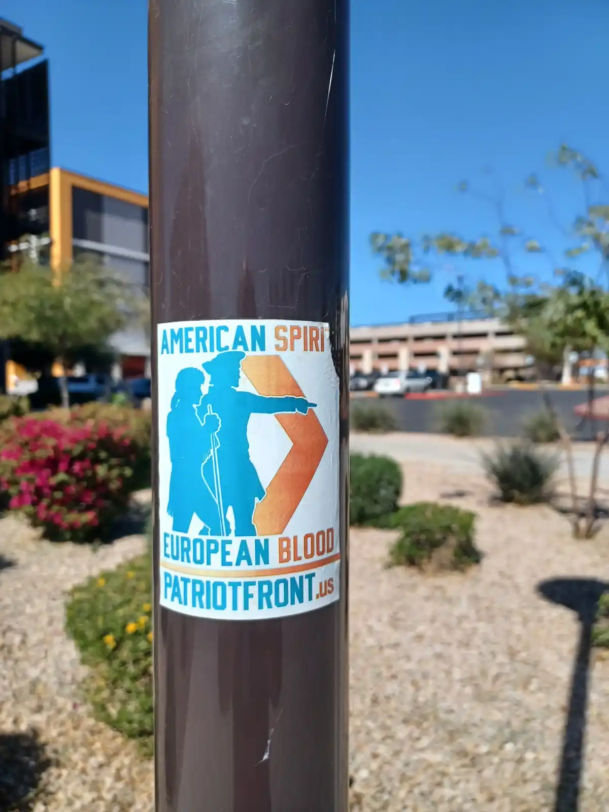 A sticker on a dark pole shows blue silhouettes of a Native American and a colonial figure pointing forward, with text…