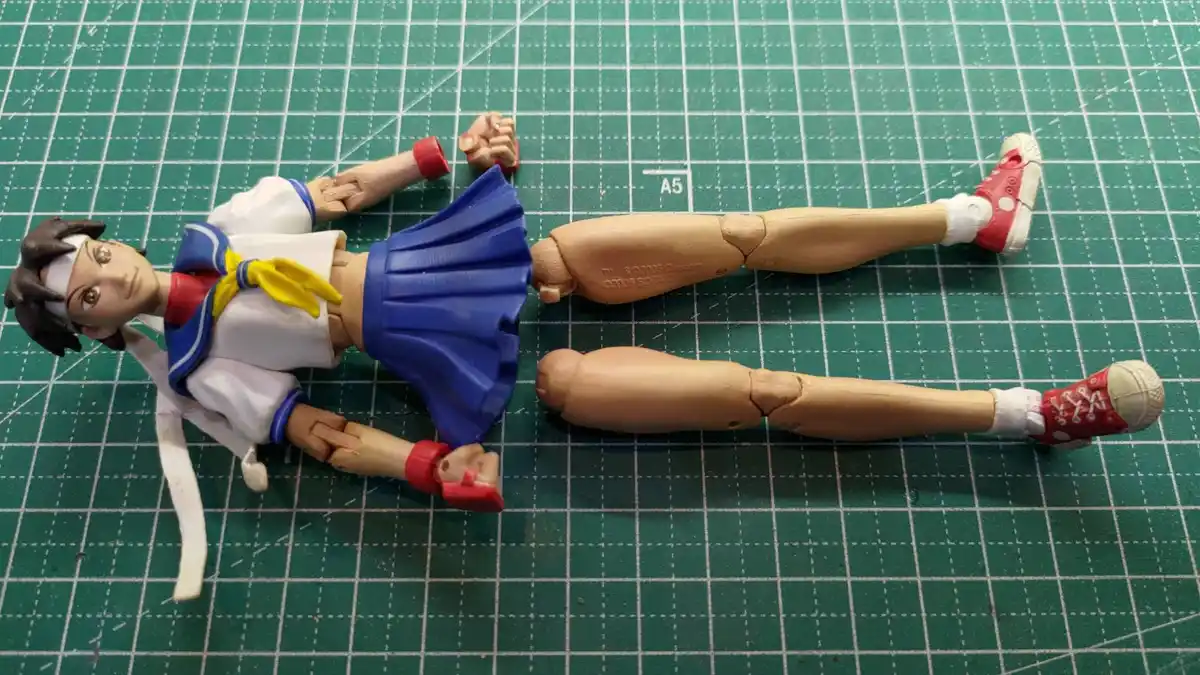 A disassembled anime-style action figure, likely from the 'Tennis no Oujisama' series, lies on a green cutting mat with its…