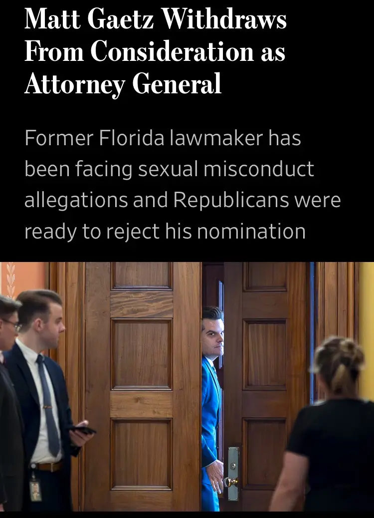 A man in a blue suit peeks out from behind a wooden door in a formal setting, looking surprised or caught off guard…