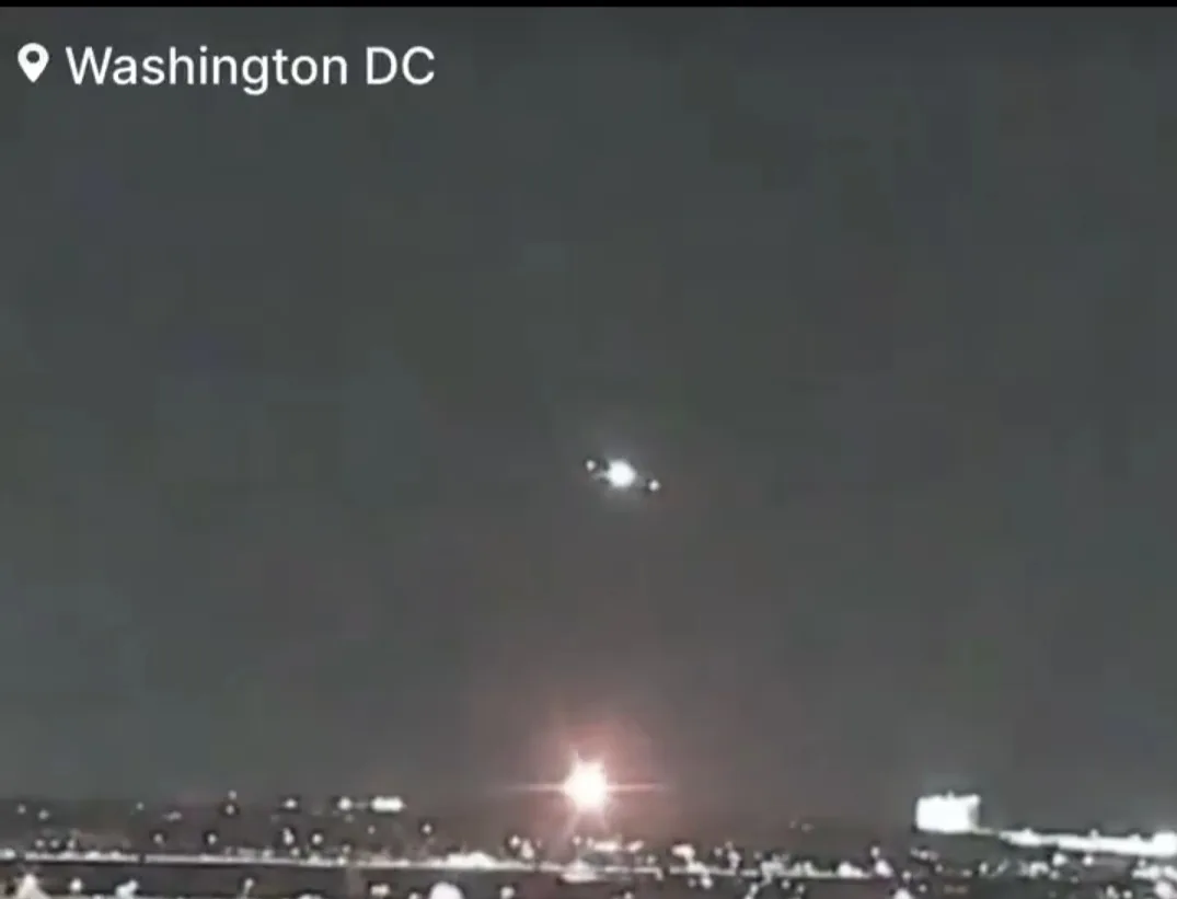 A grainy night-time video shows a bright, blurry object with multiple lights hovering in the dark sky above a cityscape…