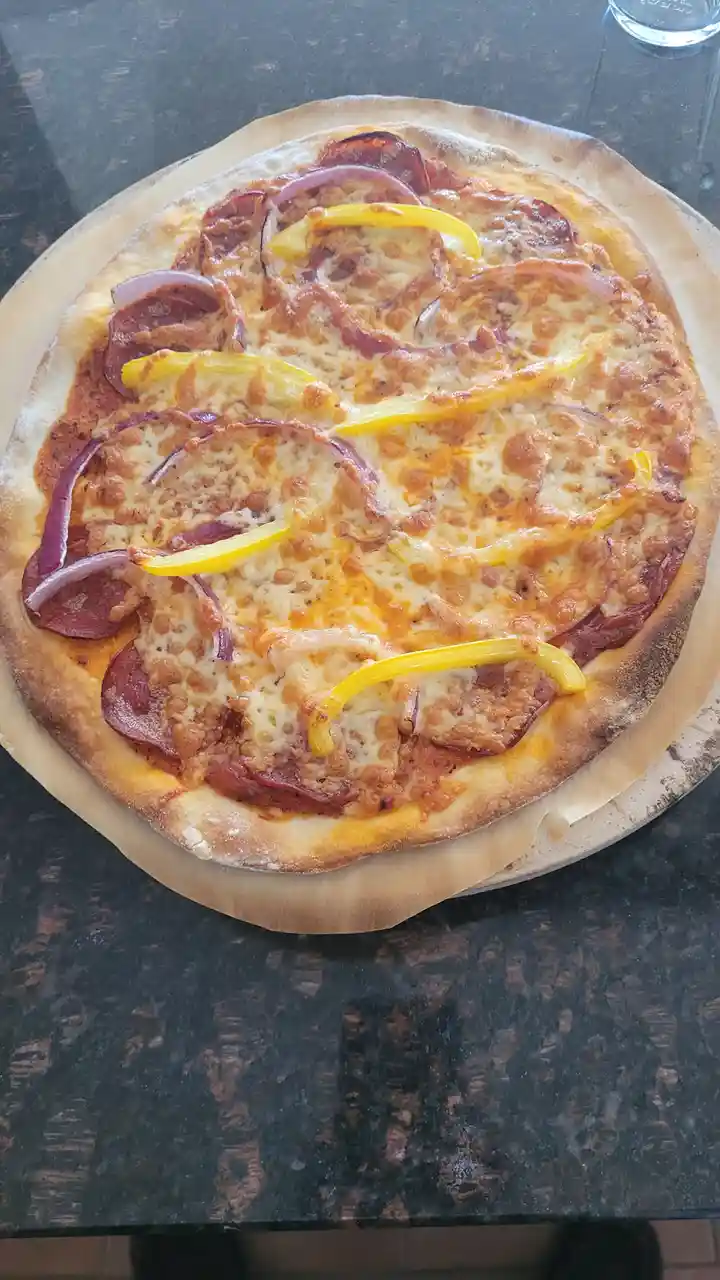 A freshly baked pizza with pepperoni, red onions, and yellow bell peppers sits on parchment paper atop a dark countertop…