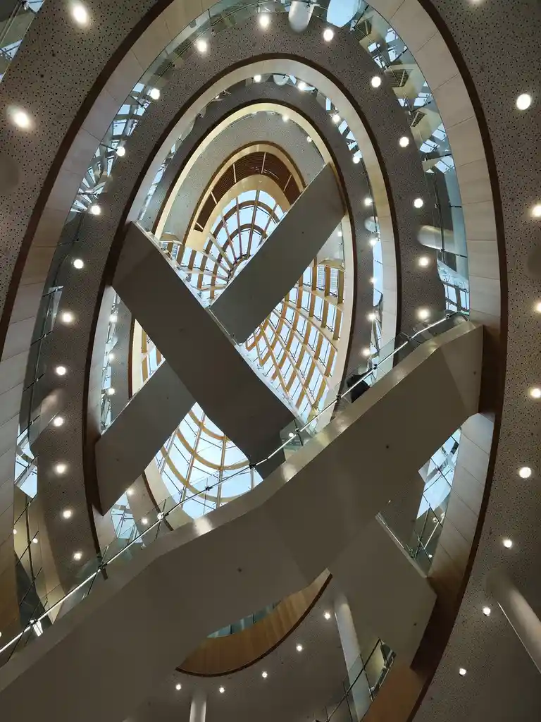 A low-angle photo looking up through a modern, multi-level spiral atrium with curved balconies, glass railings, and a…