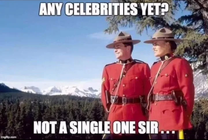 Two Canadian Royal Canadian Mounted Police officers in red uniforms and wide-brimmed hats stand side by side, looking off…