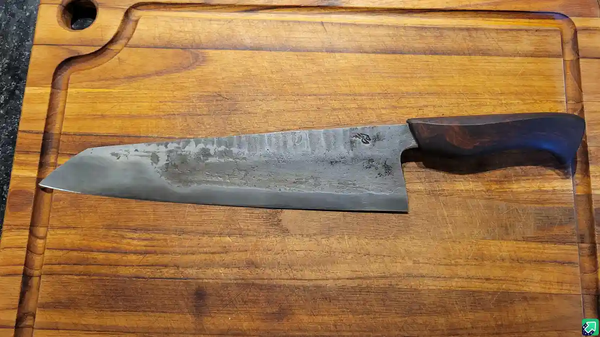 A well-used, wide-bladed chef's knife with a dark wooden handle rests horizontally on a heavily scratched wooden cutting…