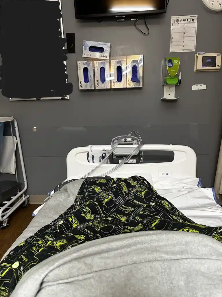 A hospital bed with a Star Wars-themed blanket featuring characters like Darth Vader and Stormtroopers, positioned in a…