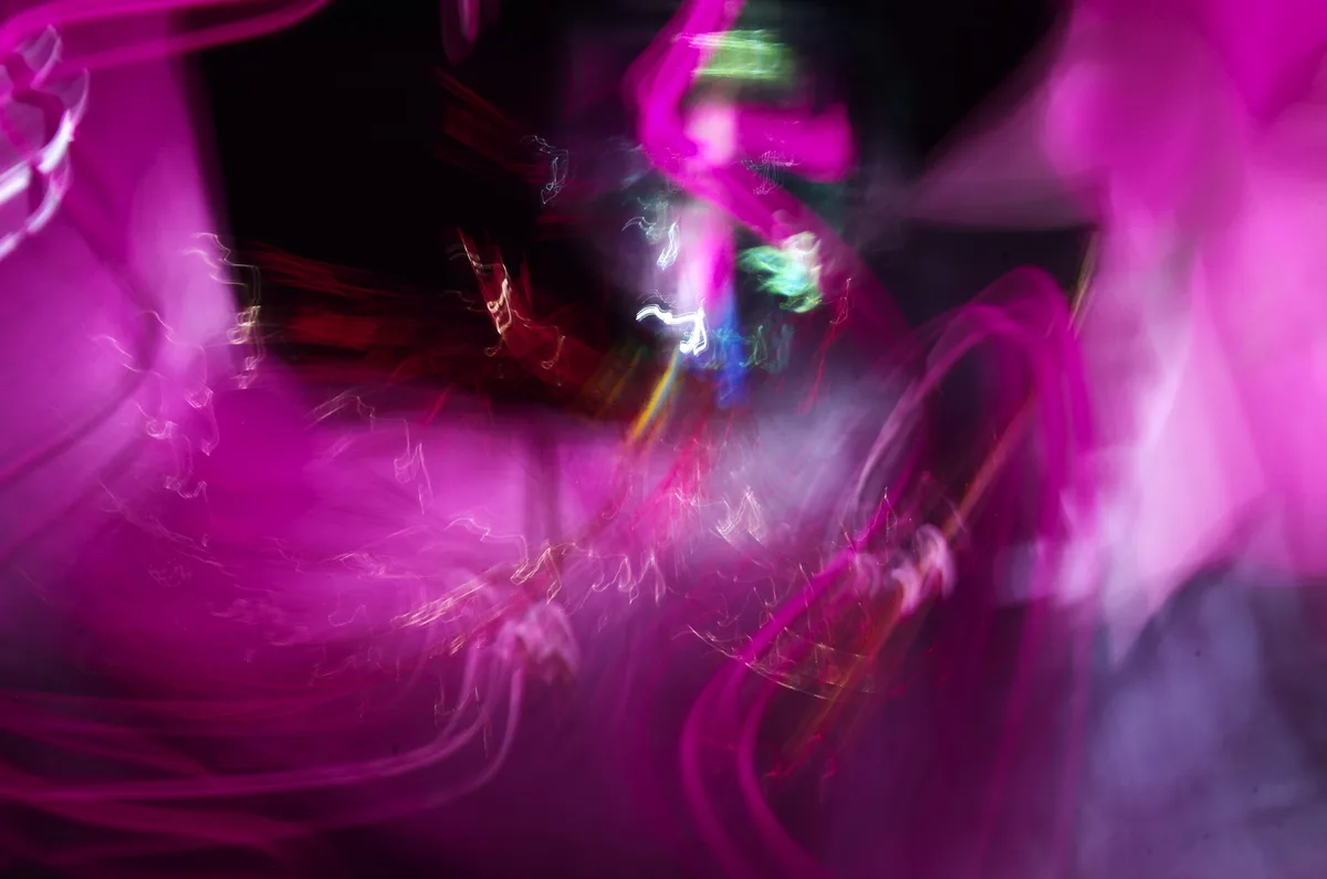 An abstract light painting image featuring swirling, blurred streaks of magenta, pink, red, and hints of green and white…