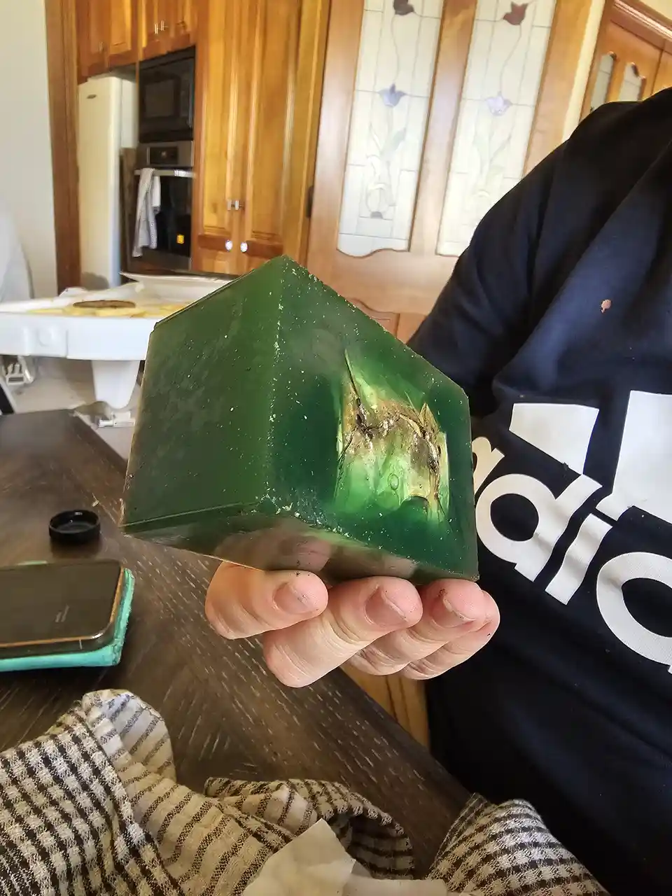 A person holds up a large, green, translucent cube of jello with a visible crack and a golden, dragon-like shape embedded…
