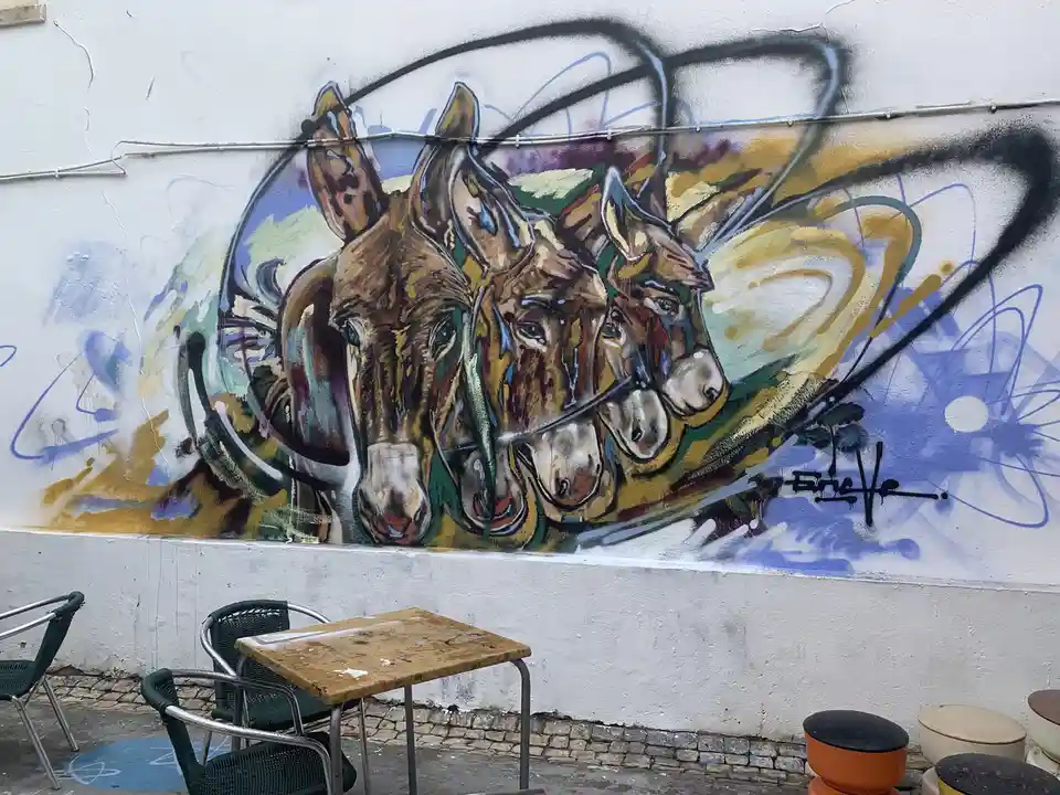 A vibrant street mural depicts three donkeys' heads in profile, painted with expressive brushstrokes and swirling abstract…
