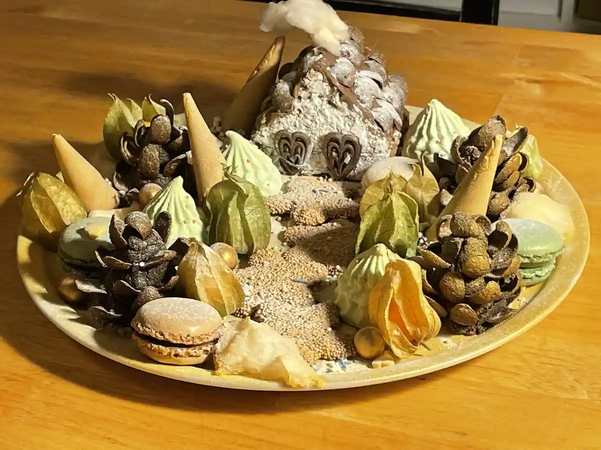 A plate of assorted pastries and confections is arranged to resemble a miniature winter scene, featuring a central…