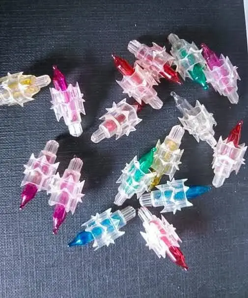 A scattered pile of small, clear plastic Christmas light bulbs with colorful glass tips in red, green, blue, pink, and…