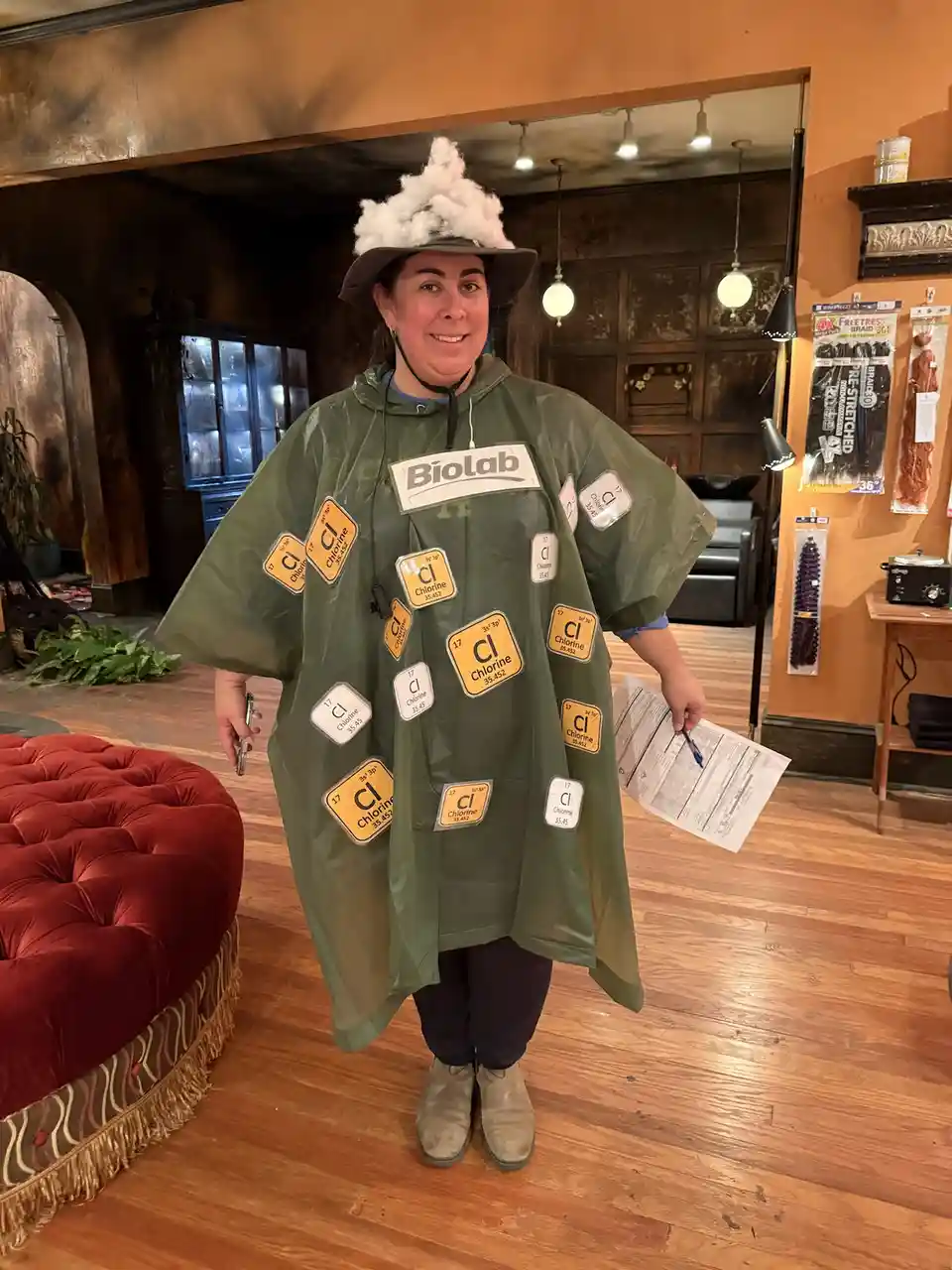 A person wearing a green plastic poncho labeled 'Biolab' is covered in multiple yellow and white stickers depicting the…