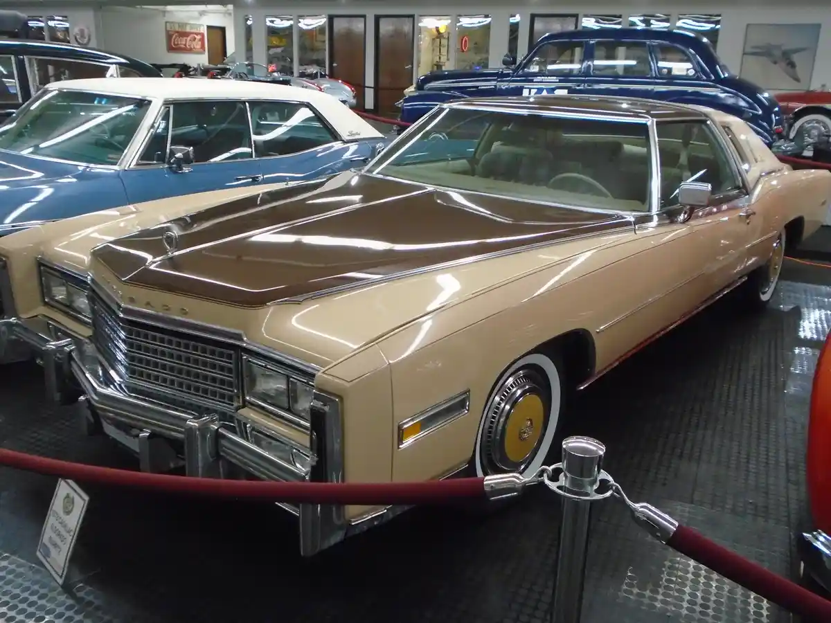 A tan and brown 1979 Cadillac Eldorado Biarritz is displayed in a museum with other classic cars behind it, roped off for…
