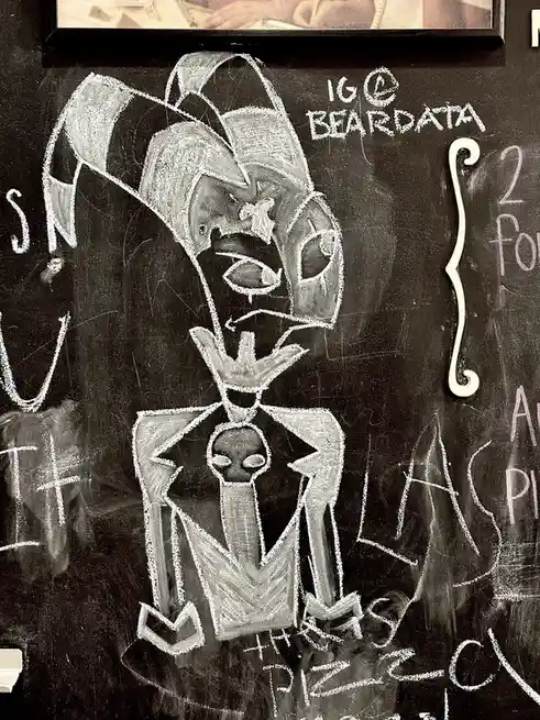 A chalk drawing on a blackboard depicts a stylized, cartoonish character with a large, angular hat, a stern expression, and…