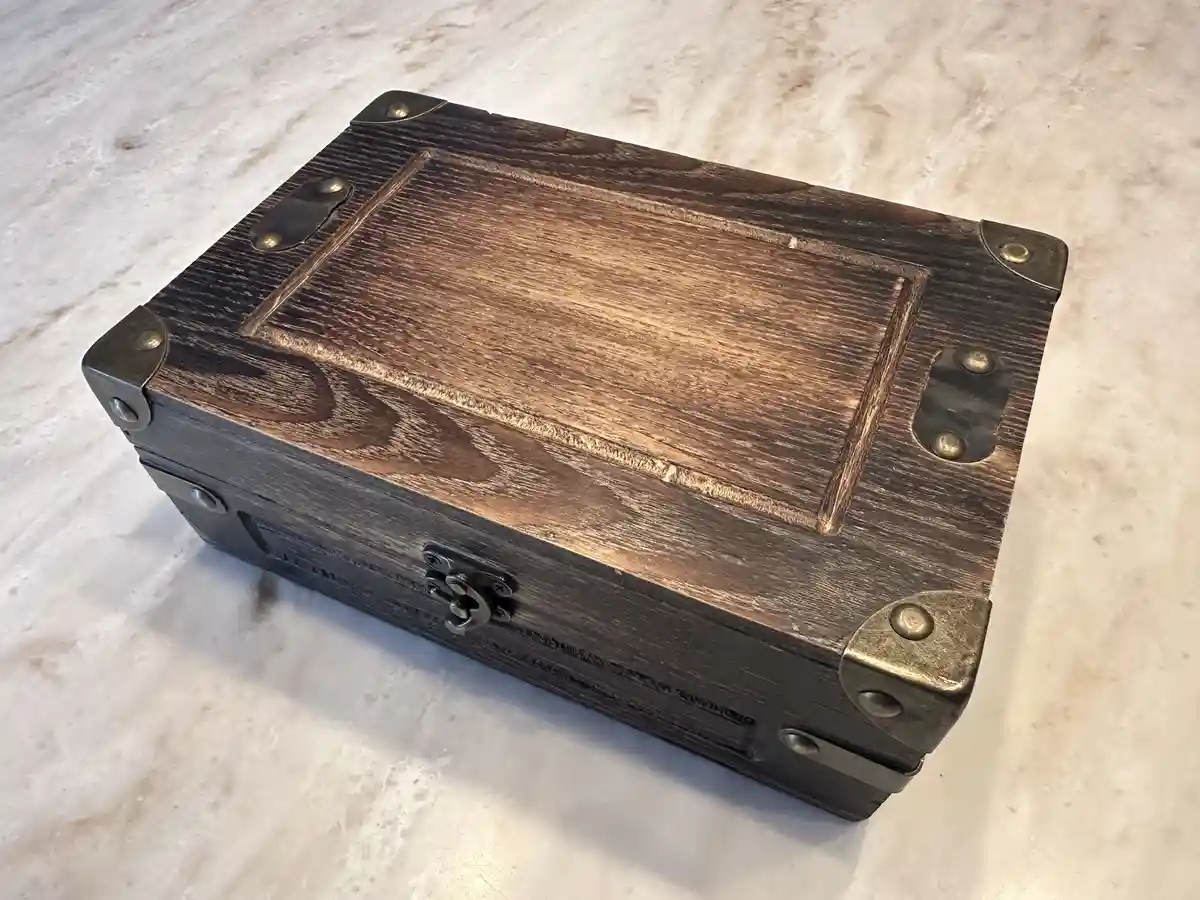 A dark wooden treasure chest with brass corner protectors and a metal latch sits on a light-colored marble surface. The…