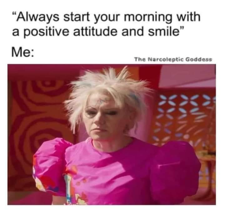 A woman with spiky, dyed blonde hair and heavy makeup wears a bright pink, puffy-sleeved shirt and looks down with a tired…