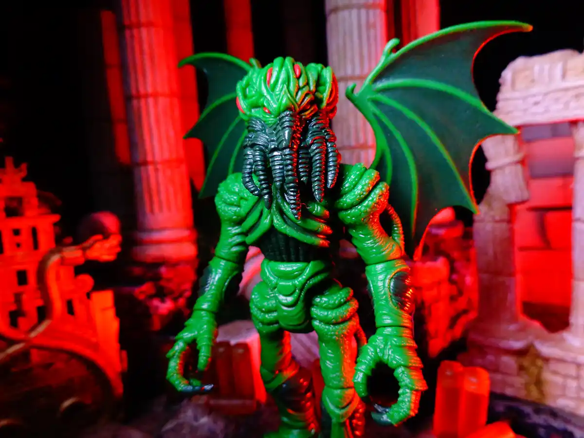 A green plastic action figure resembling a monstrous creature with bat-like wings, multiple tentacles for a face, and clawed…