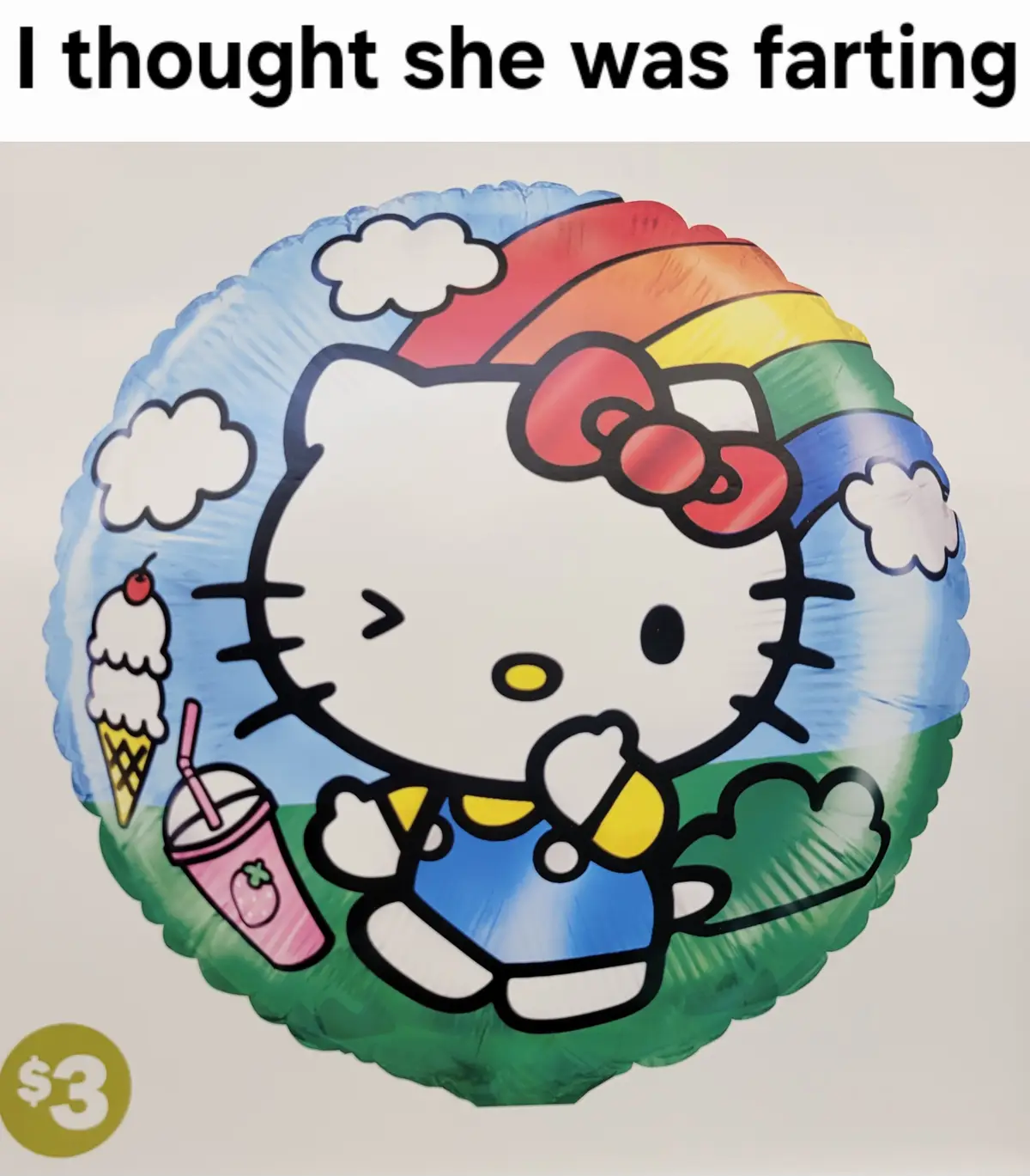A circular foil balloon features the cartoon character Hello Kitty wearing a blue outfit and red bow, sitting on green grass…