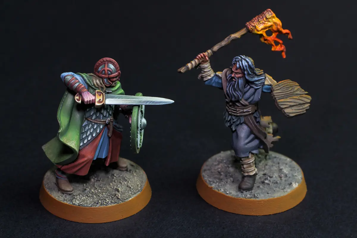 Two painted fantasy miniatures face off: one in green armor with a sword and shield, the other a bearded warrior with a…