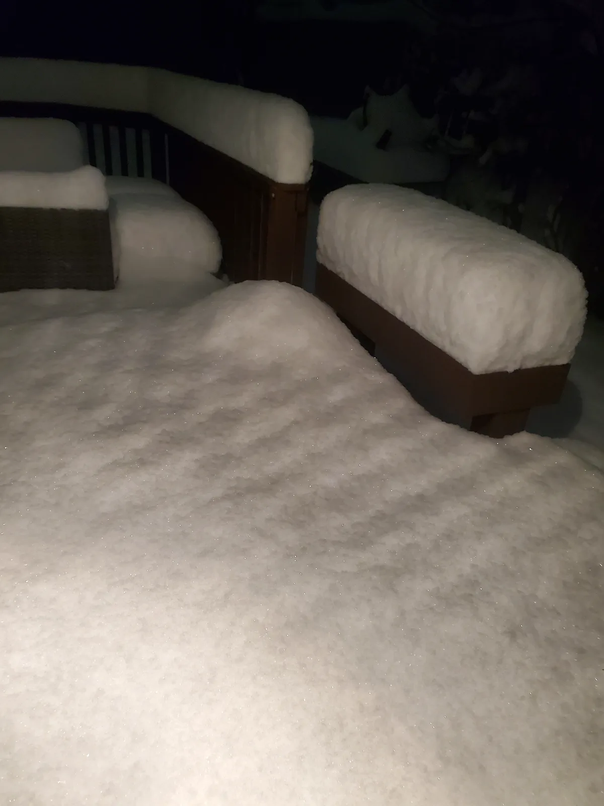 A nighttime photo shows outdoor patio furniture, including a sectional sofa and ottoman, completely buried under a thick…
