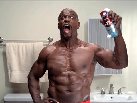 A muscular black man with a shocked expression stands in a bathroom, holding up a can of deodorant. He has a towel hanging…