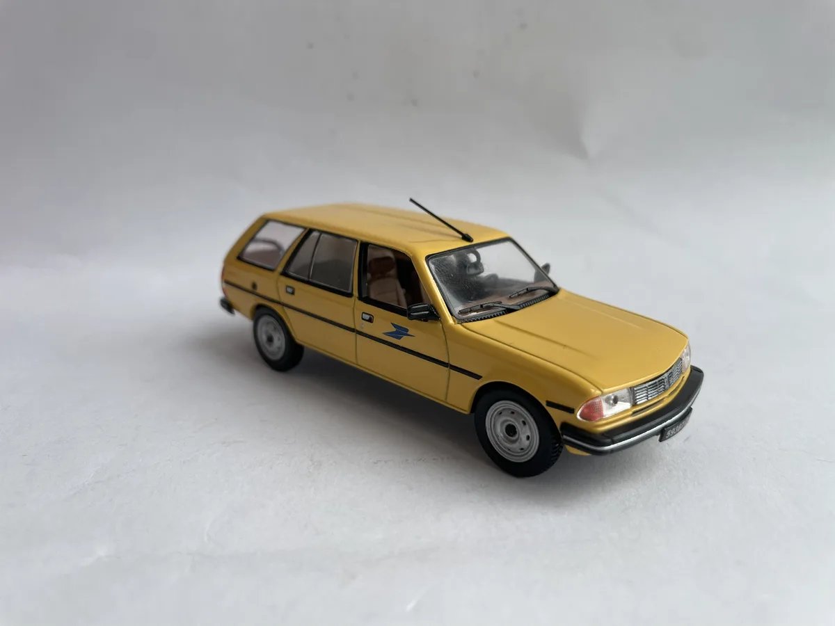 a yellow toy station wagon model car with a blue postal service logo on its side, photographed against a plain white…