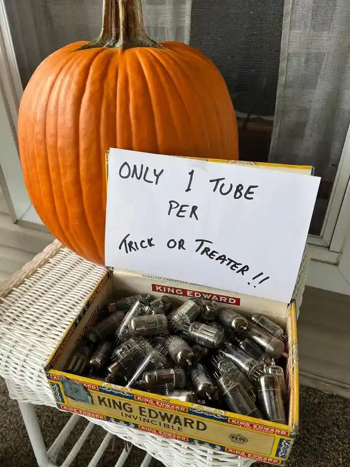 A large orange pumpkin sits behind a white wicker table holding an open vintage 'King Edward Invincible' tobacco box filled…