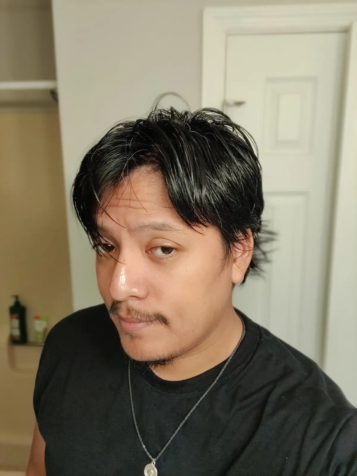 A man with dark, wet-looking hair and a mustache stares directly at the camera with a slightly annoyed or resigned…
