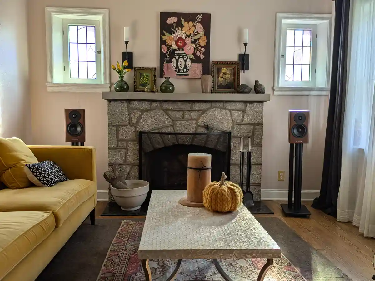 A cozy living room features a stone fireplace with decorative items, a yellow couch, and a mosaic coffee table. Two tall…