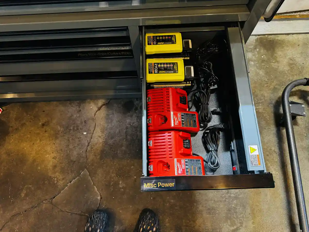 An overhead shot shows an open drawer labeled 'Misc Power' in a metal toolbox, containing four power tool batteries — two…