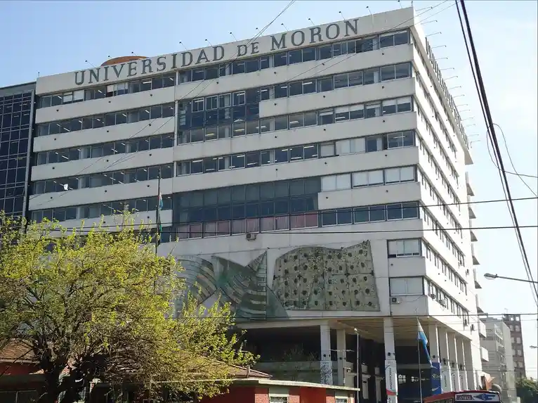 A large, multi-story white building with 'UNIVERSIDAD DE MORON' written across the top, featuring rows of windows and a…
