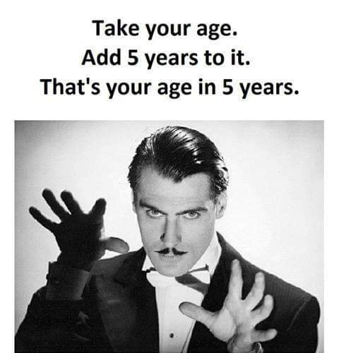 A black and white photo of a man in a tuxedo with a mustache, wearing gloves, and gesturing with both hands as if explaining…