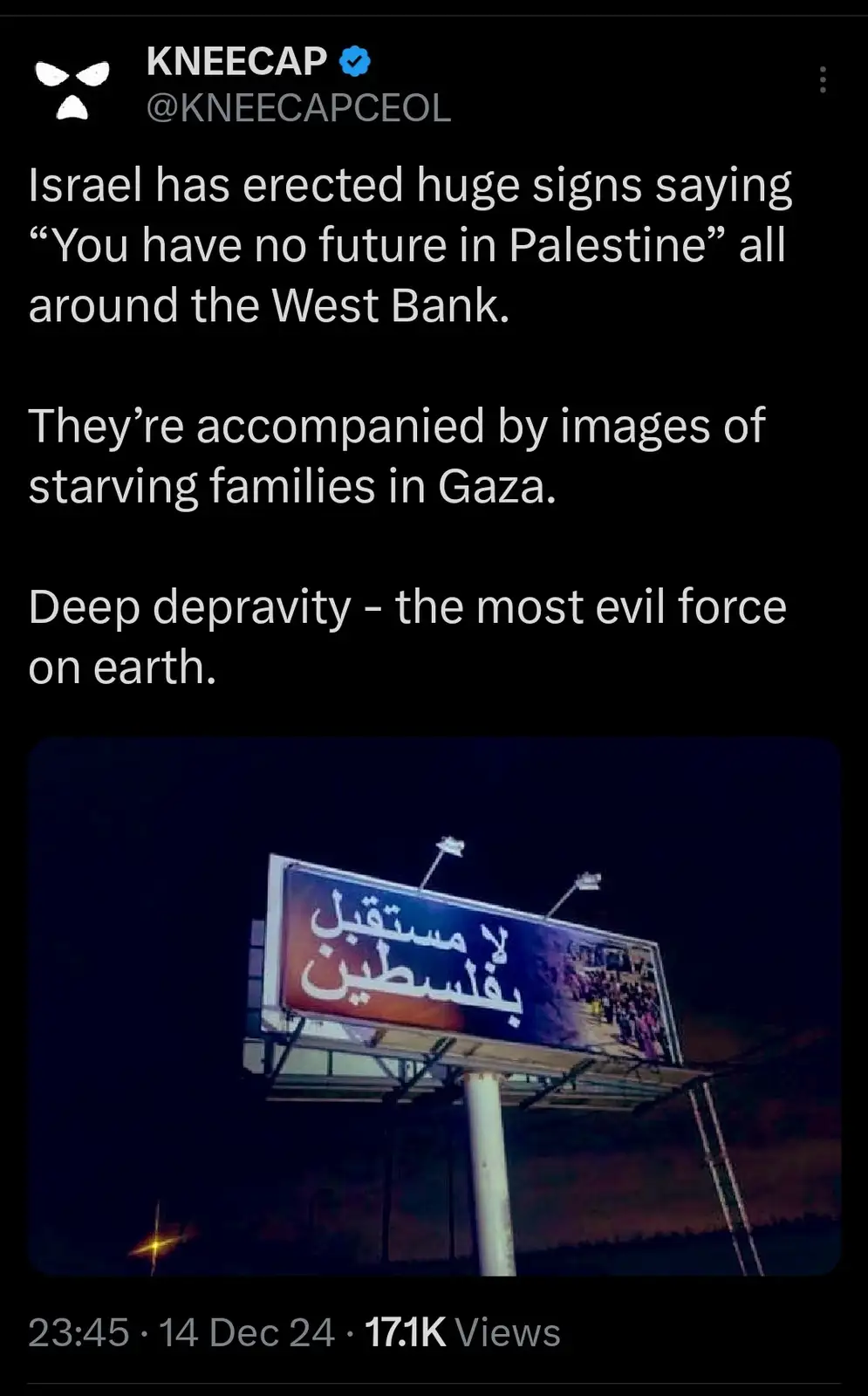 A nighttime photo of a large illuminated billboard in the West Bank displaying Arabic text and an image of a crowd. The…