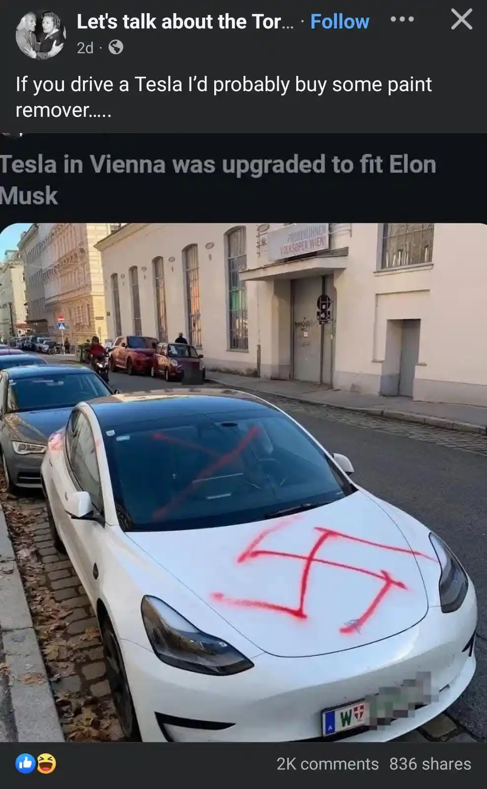 A white Tesla Model 3 is parked on a cobblestone street in Vienna, with a large red spray-painted swastika on its hood and…