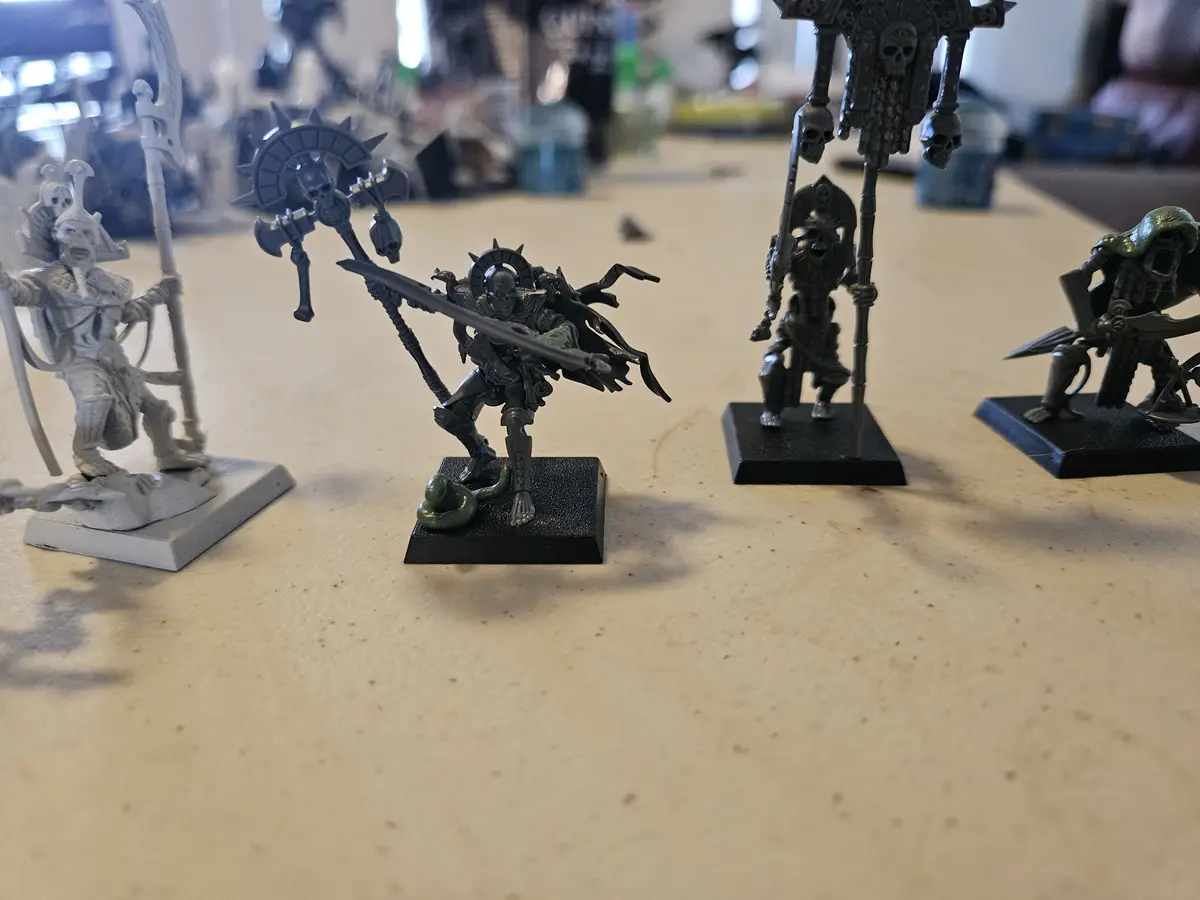 A photo of several painted miniature figurines on a table, one of which is mostly painted black with green accents and has a…