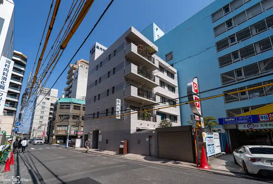 A street-level photo of a gray, multi-story building with Japanese characters reading '島内科医院' (Shimano Internal Medicine…