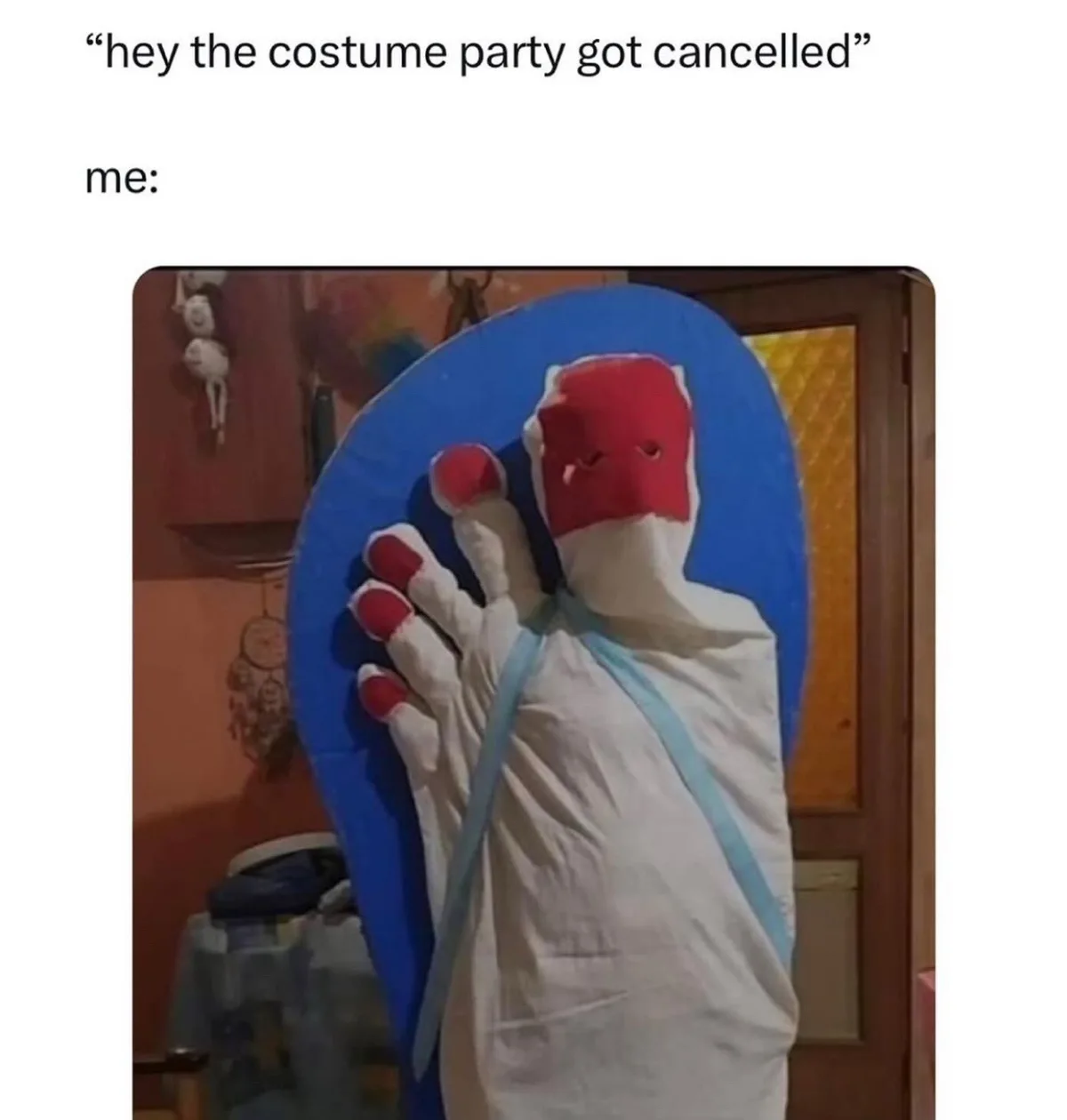 A person is dressed in a full-body costume resembling a giant blue flip flop with a red and white foot-shaped head, standing…