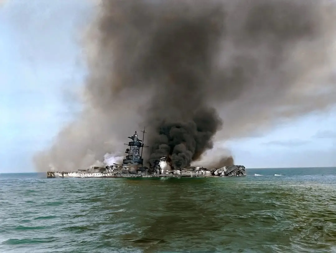 A large battleship is visibly sinking in the ocean, with thick black smoke billowing from its burning structure and water…