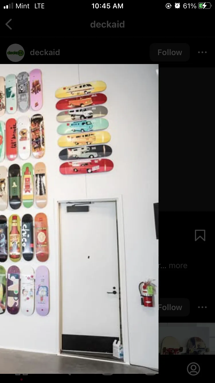 A white door is centered in a room with a white wall covered in colorful skateboards. On the left, skateboards are mounted…