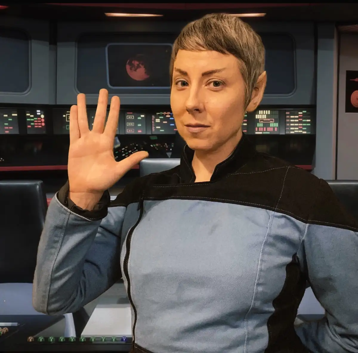 A person with pointed ears and short hair, wearing a blue and black Star Trek uniform, stands in a spaceship bridge setting…