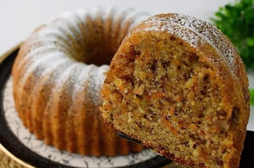 a close-up photo of a golden-brown bundt cake dusted with powdered sugar, with a slice cut out and held up to show its…
