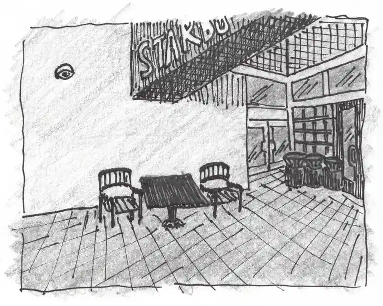 A black-and-white sketch depicts an empty outdoor seating area in front of a building with a sign reading 'STAKDU'. A single…