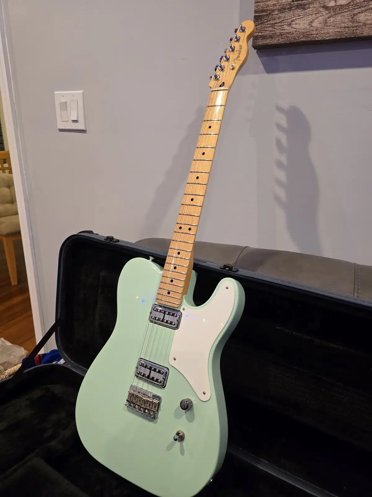 A mint green Fender Telecaster-style electric guitar with a white pickguard rests inside its open black case, leaning…