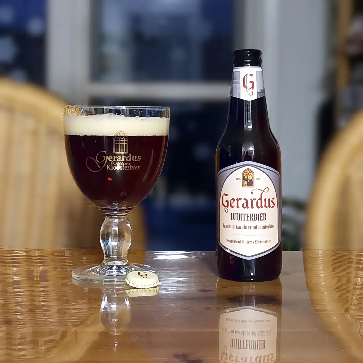 A dark, frothy Gerardus Winterbier beer is poured into a branded glass next to its bottle on a wooden table, with a bottle…