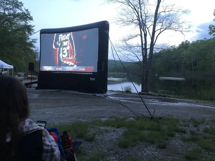 An outdoor movie screening setup with a large inflatable screen displaying the 'Friday the 13th' movie poster, set beside a…