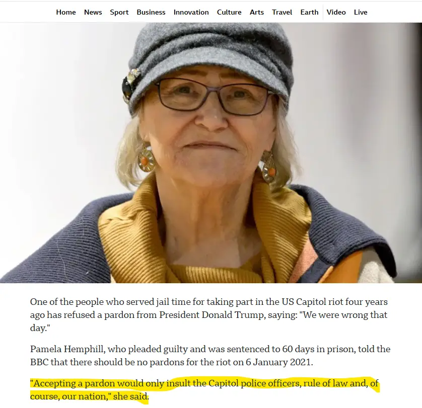 A close-up photo of an older woman wearing glasses, a grey hat, and a yellow scarf, looking directly at the camera with a…